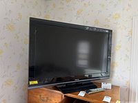 Front view of the Toshiba flat screen TV showing the screen, stand, and remote control placed on a wooden dresser.