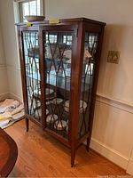 Full view of the vintage wooden display cabinet with glass doors, lattice pattern, and mirrored back