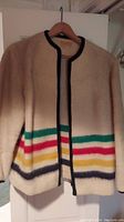 Full view of wool Hudson Bay jacket hanging, showing cream color, black trim, and multicolor stripes