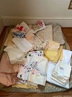 Overview of assorted vintage table linens including embroidered, crocheted, and lace edged pieces, as well as printed tea towels and napkins.