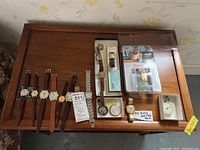 Photo showing the full lot of thirteen watches including wristwatches with leather and metal bands, dismantled pocket watch parts, and packaged stopwatch on a wooden tray.