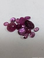 Close-up of multiple loose faceted rubies in shades of red and pink on a white background.