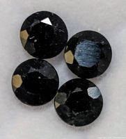 Close-up of four round faceted blue sapphire gemstones with light reflections seen on polished facets.