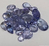 Loose genuine tanzanite gemstones scattered on a white surface showing multiple shapes and blue-violet hues.