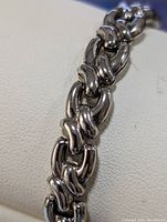 Close-up image showing the chunky, interlocking links of the silver bracelet with high polish finish.
