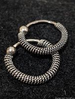 Two silver textured coil hoop earrings placed on a black background, showing the detailed coil wrapping and ball clasp.
