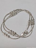 Silver necklace arranged in loops showing bead clusters and chain details.