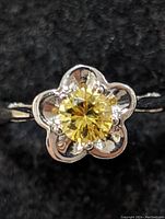 Close-up front view of silver ring showing flower design with yellow gemstone center.