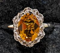 Close-up view of silver ring with an oval amber-colored faceted stone set in a textured silver border on a black background.