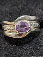 Close-up front view of sterling silver ring with oval amethyst center stone and diamond accent stones on band.