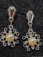 Front view of the pair of silver earrings with pearl and stone accents on a black background.