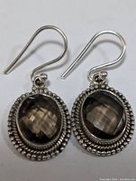 Front view of the pair of sterling silver earrings with faceted oval smokey quartz stones and detailed bezel setting against white background.