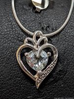Front angle close-up of sterling silver heart pendant with white topaz center stone and decorative detailing.