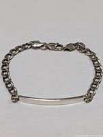 Top view of sterling silver bracelet showing curb chain links and rectangular ID plate on white background.