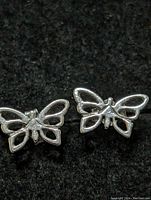 Photo showing two sterling silver butterfly earrings lying side by side on a dark surface, highlighting their openwork wing design and shiny silver finish.