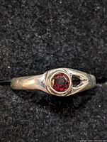 Front view of sterling silver ring with round garnet stone on black fabric background.