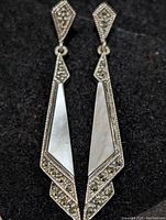 Pair of sterling silver long drop earrings shown front view on dark background, highlighting geometric shapes, marcasite stones and mother of pearl inlays.