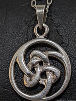 Close-up of the round sterling silver pendant showing the woven knot design and chain attachment.
