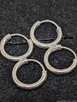 Four sterling silver hoop earrings arranged on a black surface showing polished finish and latch fastening mechanism.