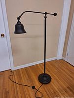 Full view of the floor lamp showing the adjustable arm, dome-shaped shade, and round base on a hardwood floor.