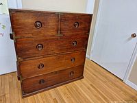 Full view of the wooden antique campaign cabinet showing five drawers with inset circular handles and brass corner reinforcements.