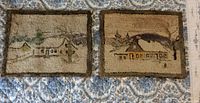 Both antique hand hooked mats displayed side by side on a blue and white patterned fabric. Each shows a rustic winter house scene and a colored border. Mats appear faded and aged.