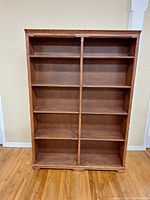 Full front view of wooden bookcase showing two vertical sections with multiple shelves on hardwood floor.
