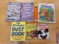 Photo showing six children's books laid out on a wooden surface, including novels and activity books in good condition.