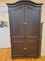 Front view of the tall dark wood cabinet with four paneled doors and glass knobs.