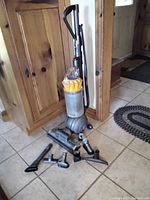 Dyson upright vacuum cleaner with multiple attachments laid out on tile floor.
