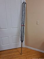 Folded clothes line with all cords wrapped neatly around the pole, positioned upright against a door.