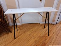 Full view of the white folding workbench with black metal legs, showing overall condition and structure.