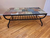 Full view of rectangular coffee table showing multicolored tile top and curved metal legs on hardwood floor.
