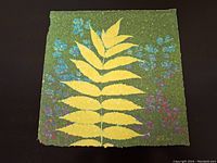 Full front view of the square paper pulp artwork showing leaf and flower stencil design in various colors on a green textured background.