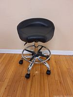 Front view of the black rolling stool showing its padded seat and chrome base with caster wheels.