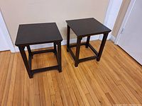 Pair of dark wood side tables positioned on hardwood floor next to beige walls and white trim