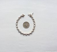 Topside view of the sterling silver tennis bracelet with clear stones and a quarter coin for size comparison.