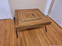 View of wooden coffee table with geometric concentric pattern on the top, showing the wood grain and layered design.