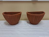Front view of two terracotta wall mount planters side by side showing ribbed design and shape