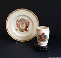 Plate and cup shown side by side on black backdrop, highlighting commemorative portraits and British flags on plate and royal crest on cup.