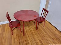 Photo of the full set showing one round table and two chairs on wooden floor against wall and door, red paint and surface wear visible.
