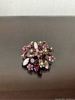 Top-down view of the brooch showcasing the clustered plum and green rhinestones and pearls in a floral motif on a reflective surface