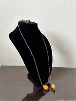 Full view of a necklace displayed on a black bust showing large oval butterscotch amber pendants with silver chain and decorative accents.