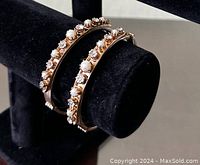 Front and angled view of both pearl and rhinestone bracelets combined on black jewelry display stand showing detail and shine.