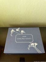 Closed box labeled Avon Mirrored Vanity featuring a navy blue box with a floral design and product name.