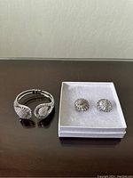 Silver rhinestone cuff bracelet next to white boxed pair of silver tone rhinestone dome earrings on black surface