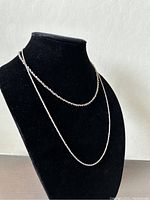Two different sterling silver chains displayed on a black bust, showing one thin delicate chain and one thicker rope-style chain.