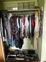 Photo showing a closet rod with about 20+ hanging vintage clothing items including dresses, tops, and jackets with several pairs of shoes in boxes below.