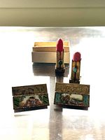 Photo of two vintage Italian sterling silver lipstick cases with detailed colored enamel panels depicting musical scenes, lipstick elements extended, placed on a reflective surface.