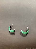 Pair of green jade and silver hoop earrings placed on a dark reflective surface.